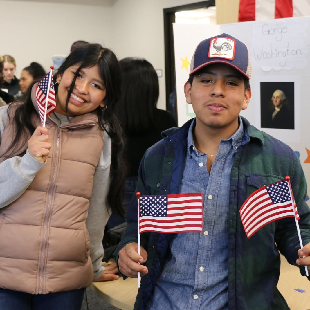  Two English learners pose with american flags in front of a presentation about George Washington